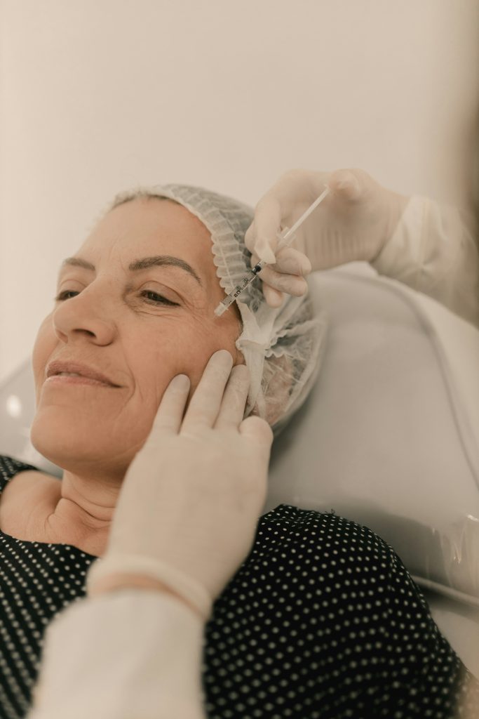 Mujer sonriente recibiendo un tratamiento de ácido hialurónico en el pómulo en una consulta de medicina estética en Valladolid